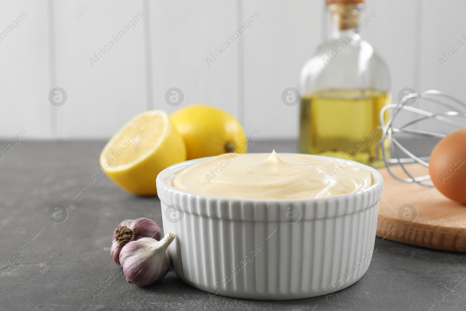 Photo of Fresh mayonnaise sauce in bowl and ingredients on grey table, space for text