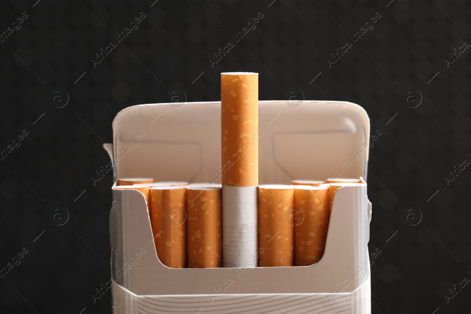 Photo of Cigarettes in pack on black background, closeup