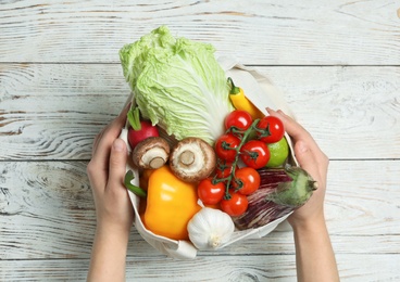 Photo of Woman holding bag full of fresh vegetables on wooden background, top view