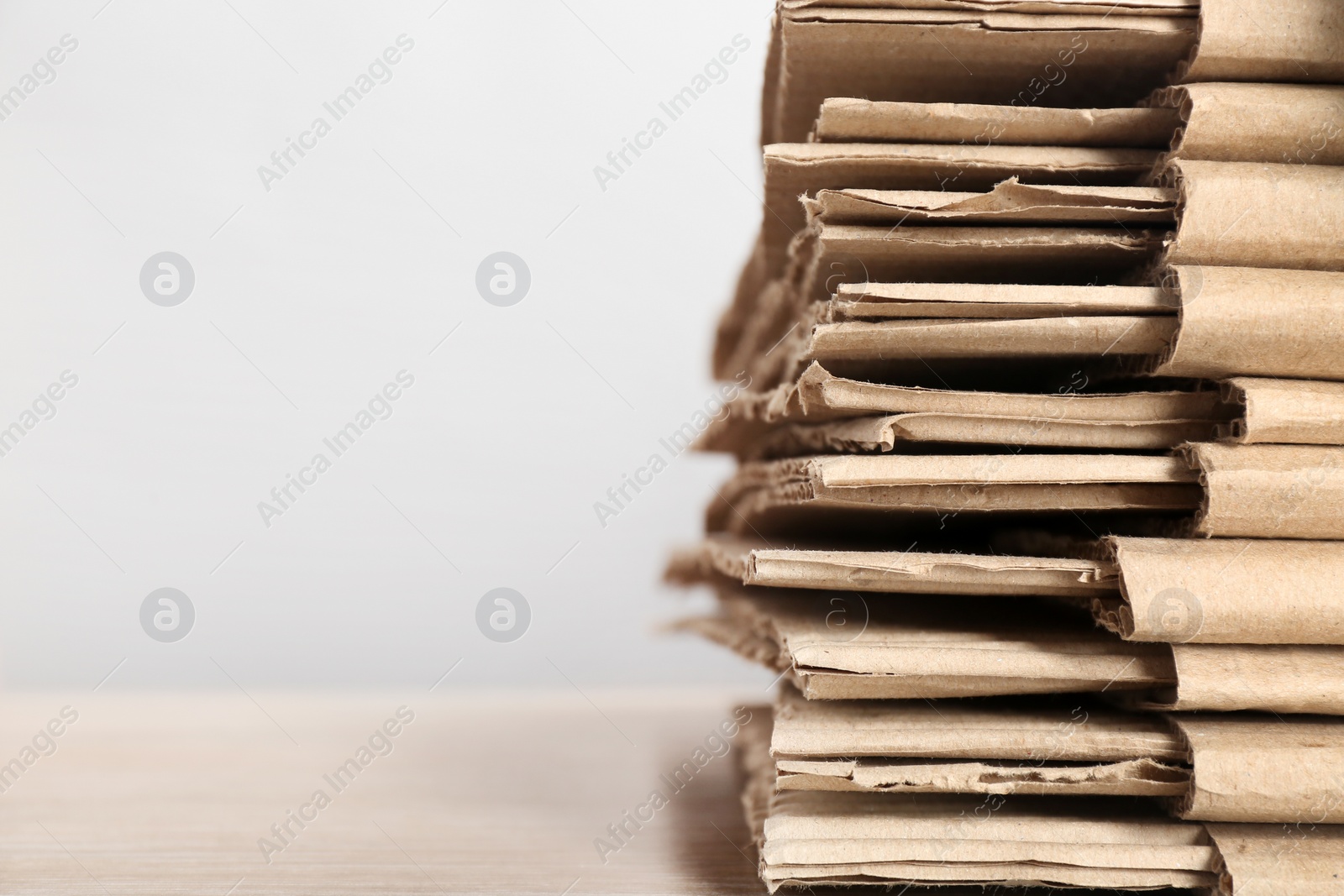 Photo of Cardboard pile on table against light background, space for text. Waste recycling concept