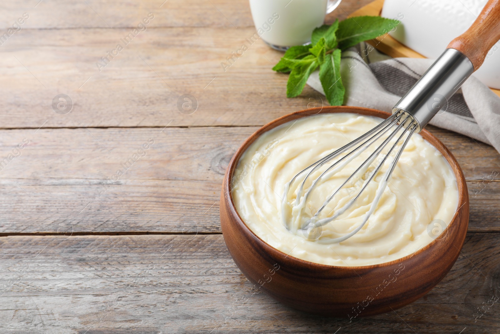 Photo of Whipping pastry cream with balloon whisk on wooden table. Space for text