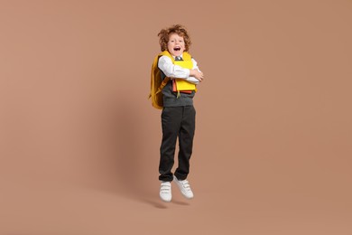 Photo of Happy schoolboy with backpack and books jumping on brown background