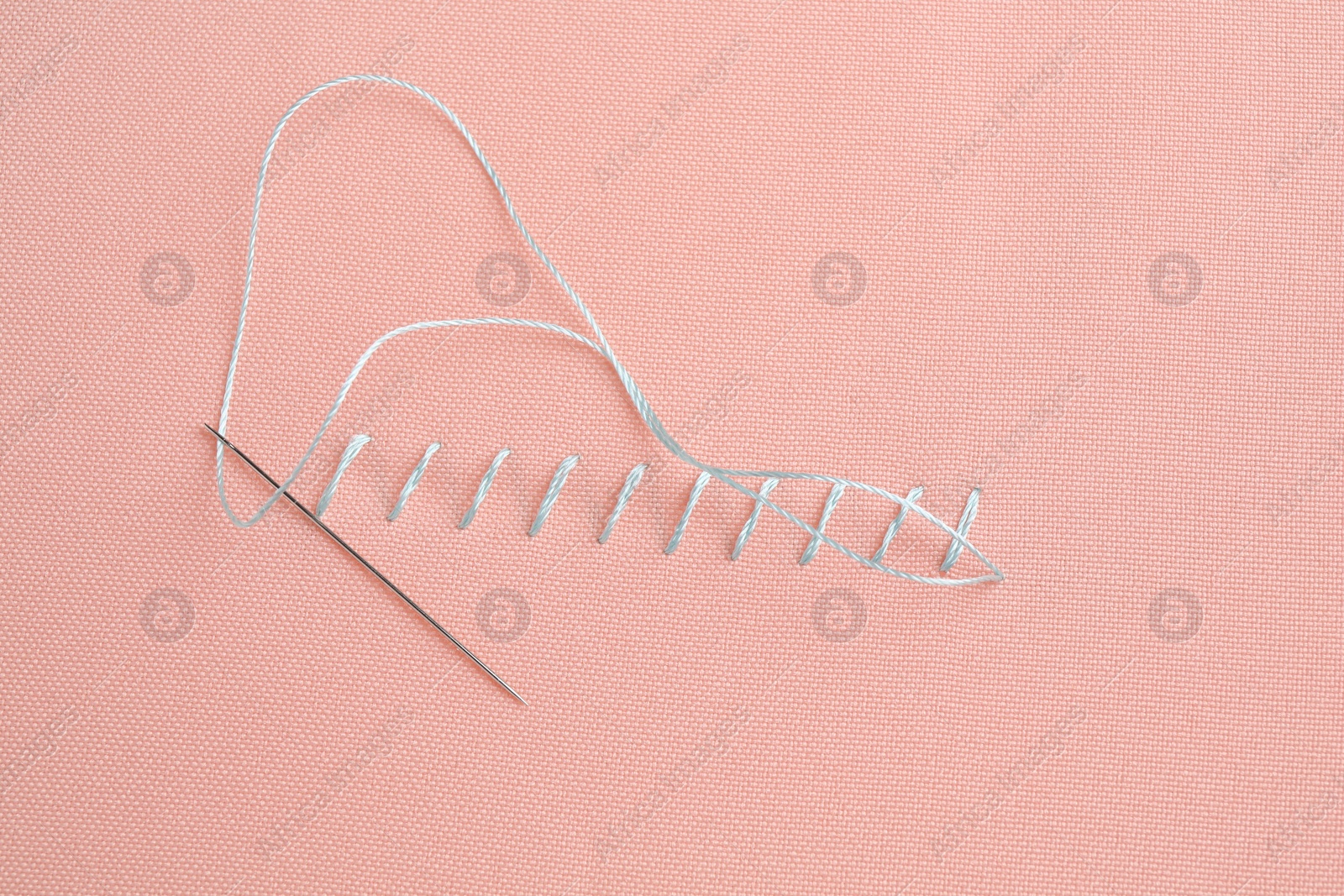 Photo of Sewing needle with thread and stitches on coral cloth, top view