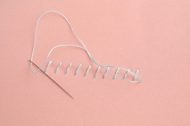 Photo of Sewing needle with thread and stitches on coral cloth, top view