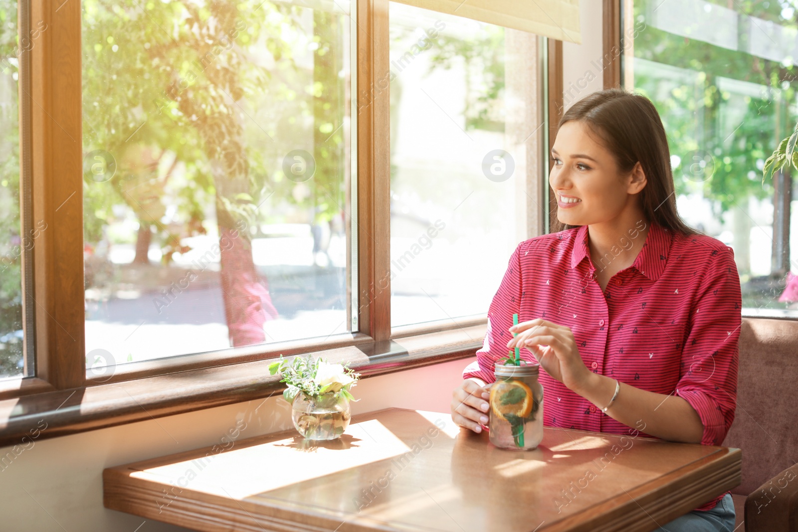 Photo of Young woman with mason jar of tasty natural lemonade in cafe. Detox drink