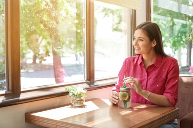 Photo of Young woman with mason jar of tasty natural lemonade in cafe. Detox drink