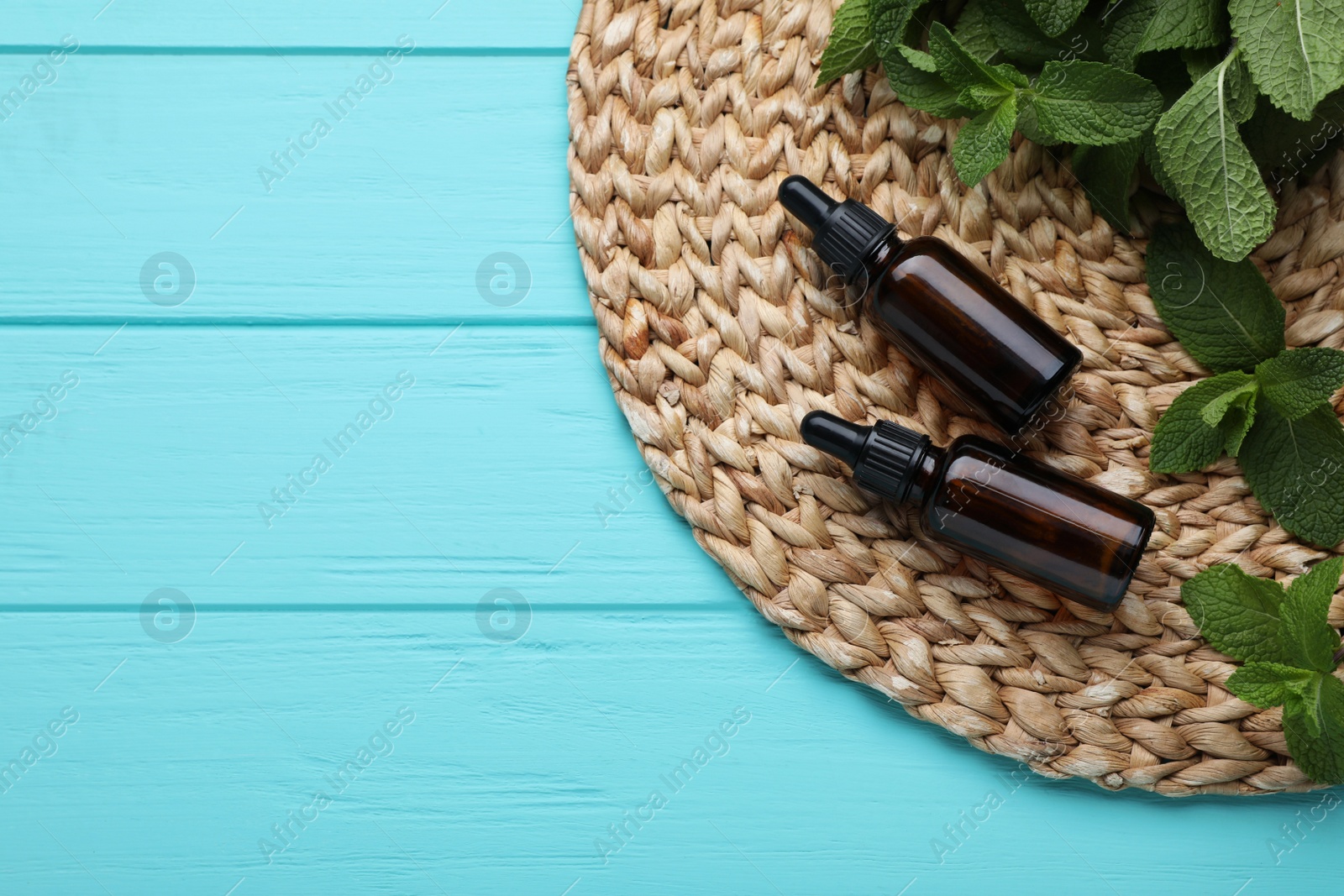 Photo of Bottles of essential oil and mint on turquoise wooden table, top view. Space for text