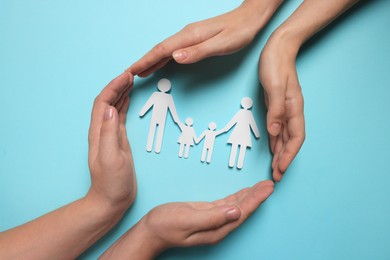 Photo of Couple protecting paper family figures on light blue background, top view. Insurance concept