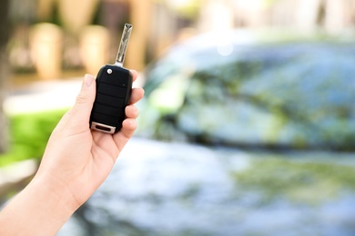 Woman holding key near new car outdoors, closeup. Space for text