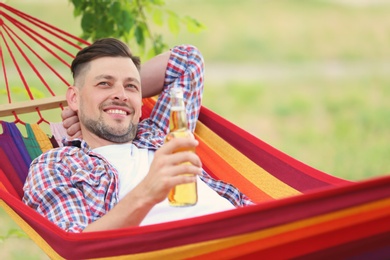 Photo of Handsome young man with bottle of beer resting in hammock outdoors