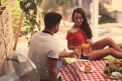 Photo of Happy couple with refreshing drink imitating picnic at home