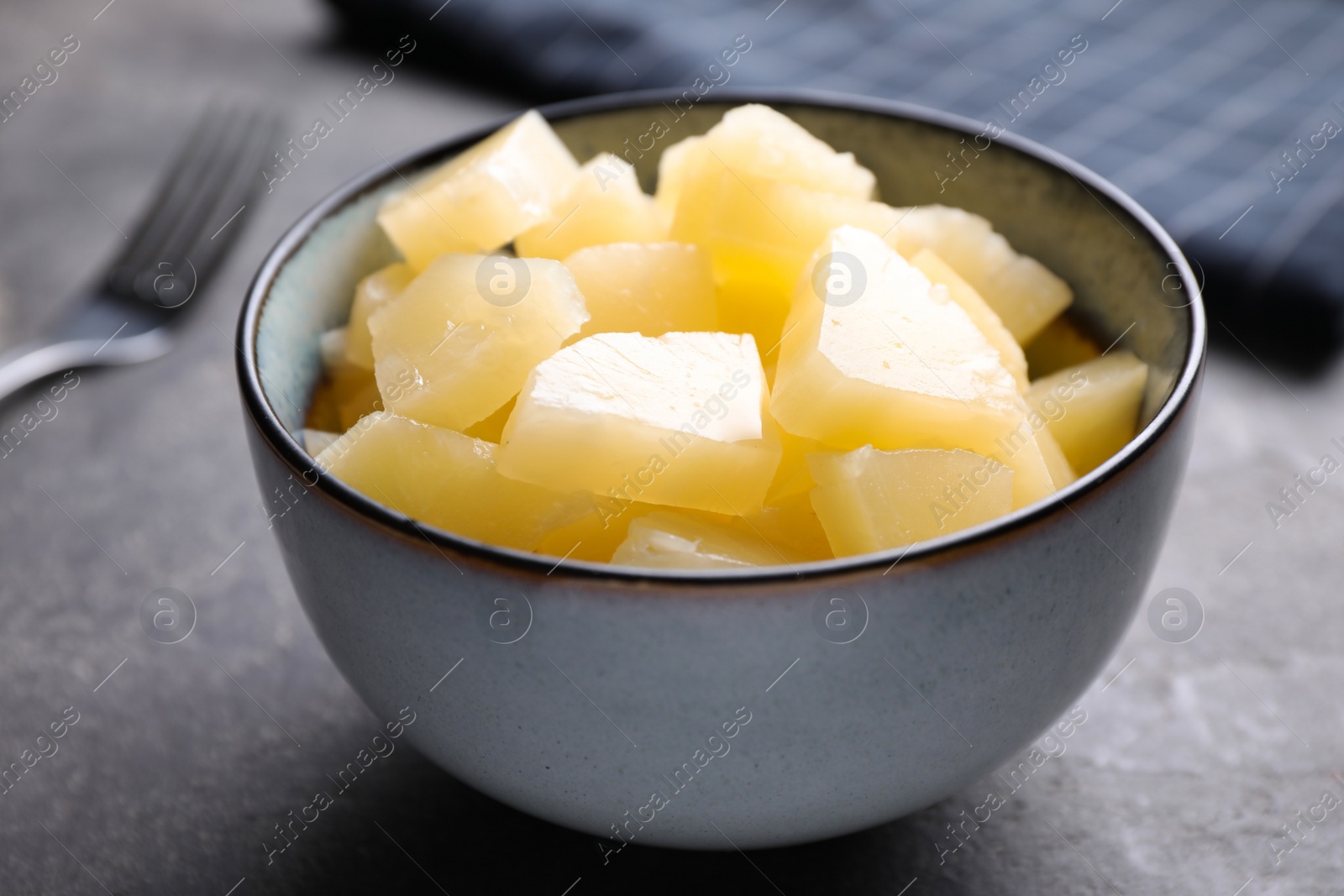 Photo of Tasty canned pineapple in bowl on grey table, closeup