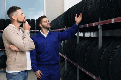 Mechanic helping client to choose car tire in auto store