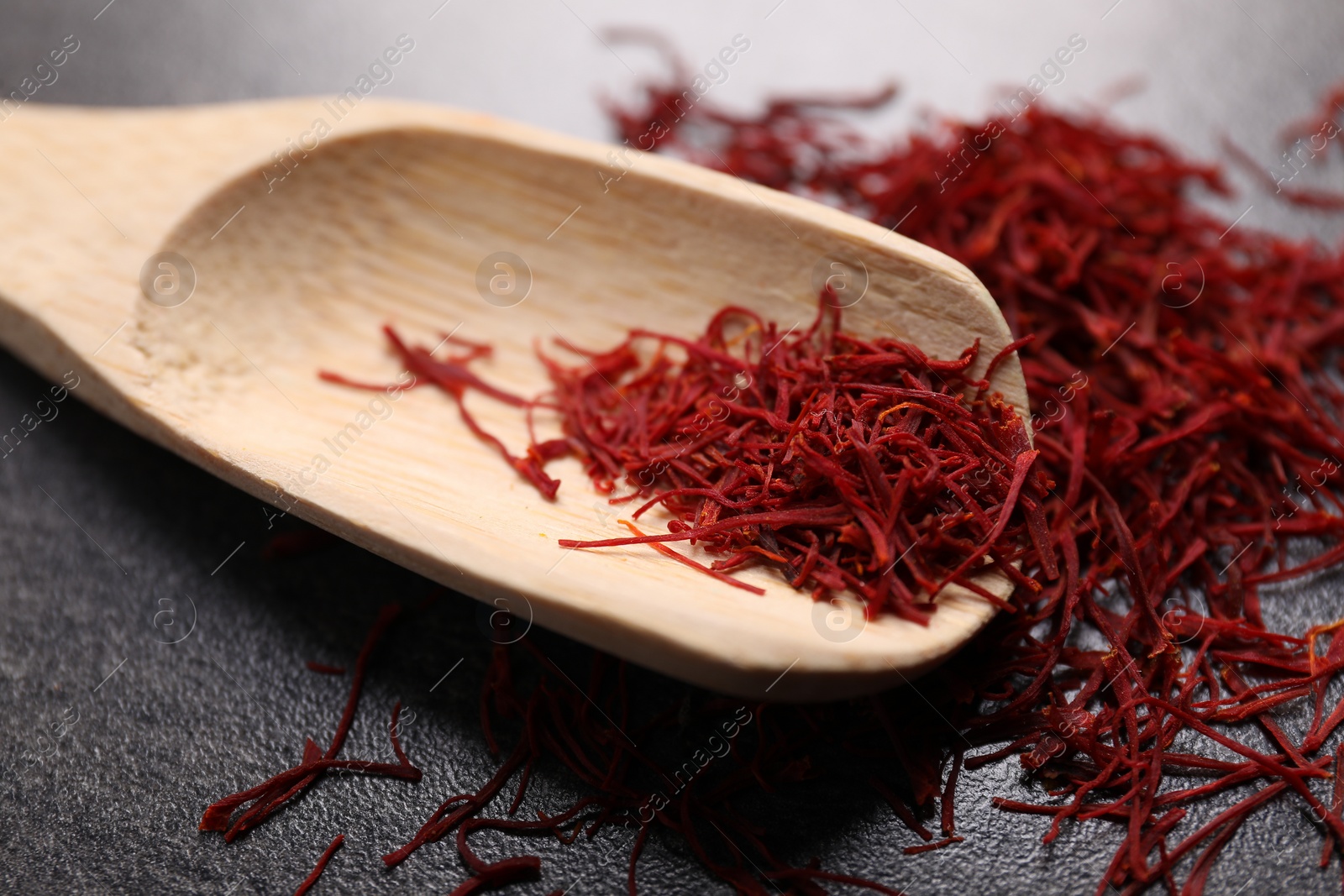 Photo of Aromatic saffron and wooden scoop on gray table, closeup