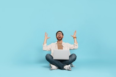 Emotional man with laptop on light blue background