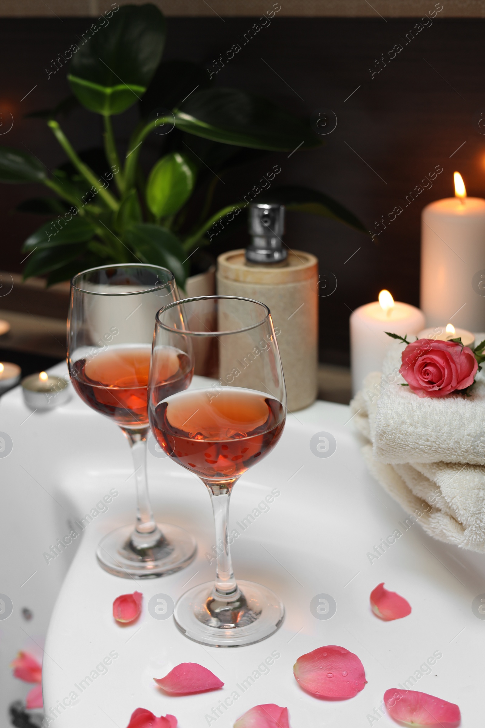 Photo of Bathtub with glasses of wine and candles indoors. Romantic atmosphere