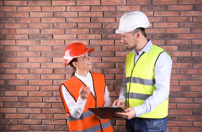 Photo of Industrial engineers in uniforms with clipboard on brick wall background. Safety equipment