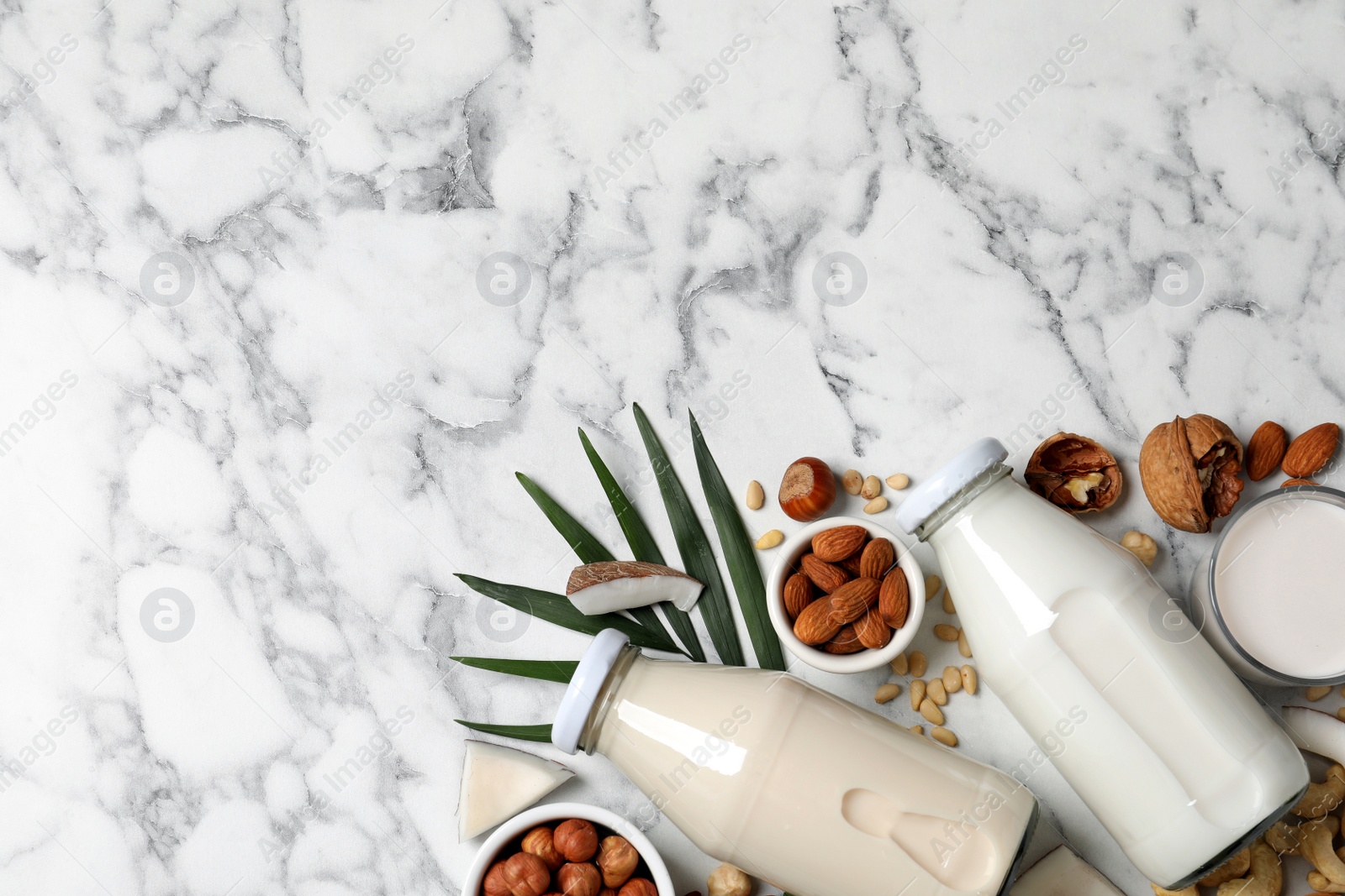 Photo of Vegan milk and different nuts on white marble table, flat lay. Space for text