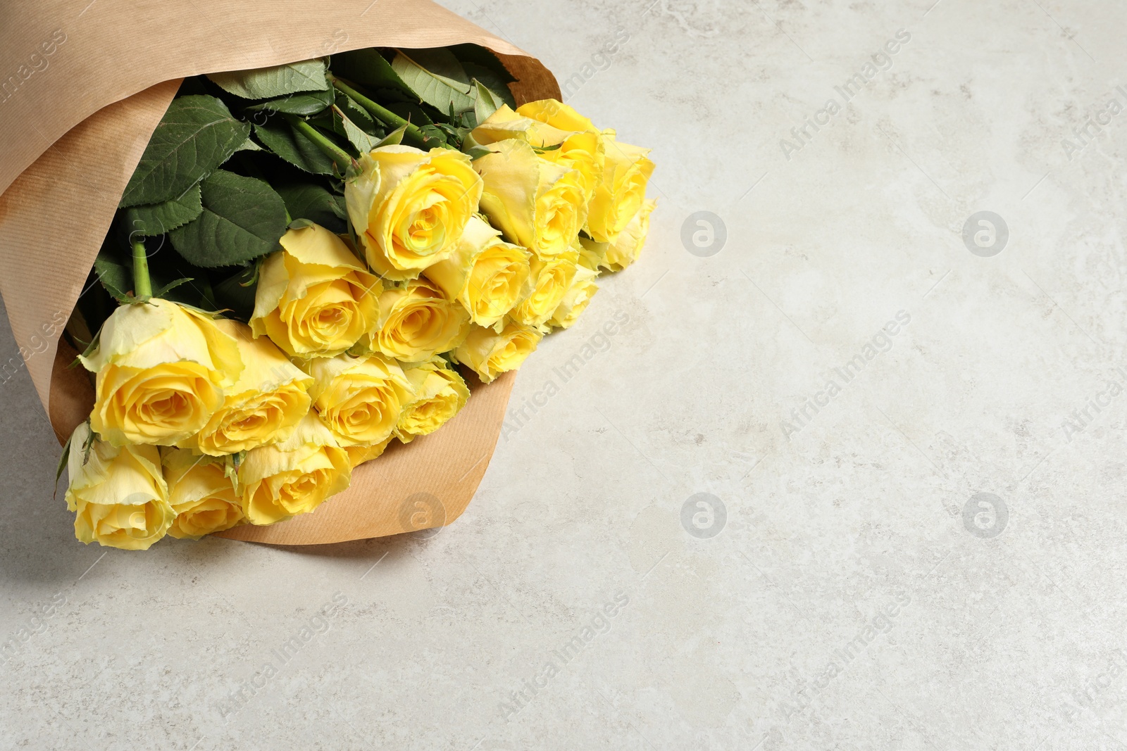 Photo of Beautiful bouquet of yellow roses on light grey table, above view. Space for text