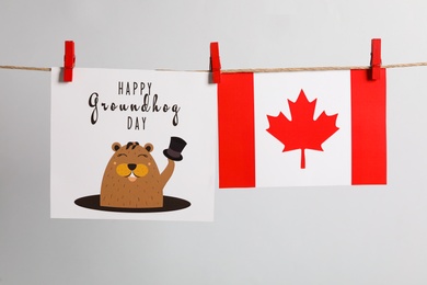 Photo of Happy Groundhog Day greeting card and Canada flag hanging on light background