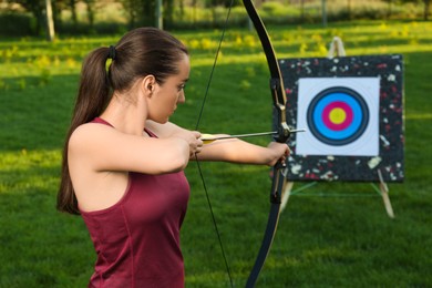 Photo of Woman with bow and arrow aiming at archery target in park
