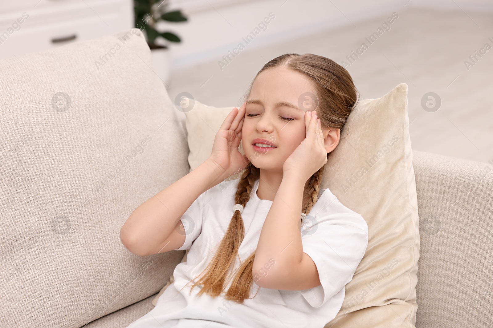 Photo of Little girl suffering from headache on sofa indoors