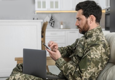 Photo of Soldier with laptop using smartphone at home. Military service