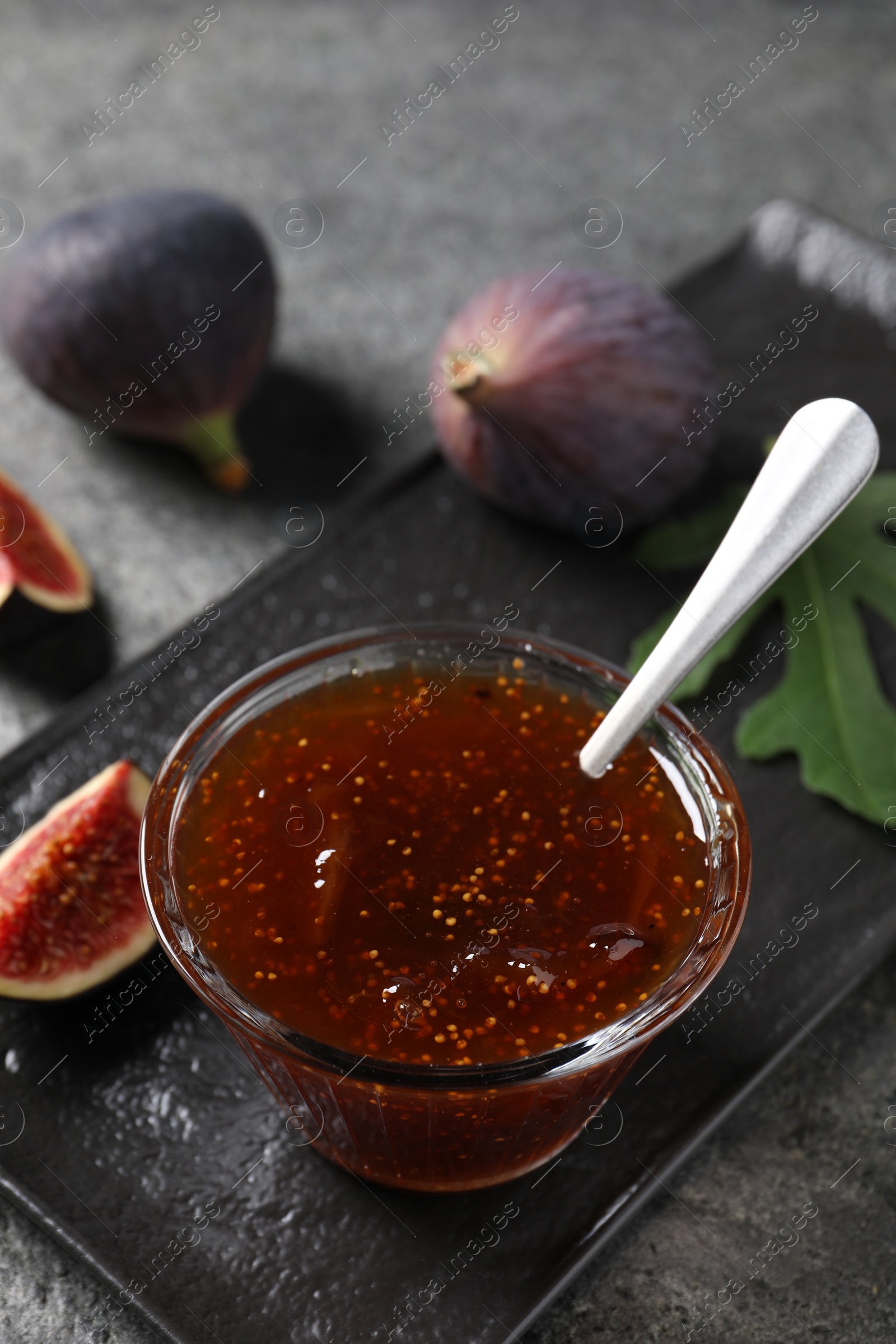 Photo of Glass bowl with tasty sweet jam and fresh figs on grey table, closeup