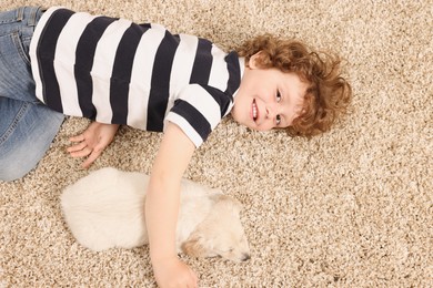 Little boy with cute puppy on beige carpet, top view