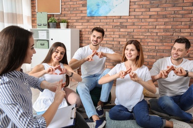 Photo of Group of young people learning sign language with teacher indoors