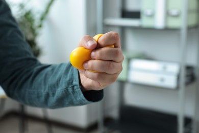 Photo of Man squeezing antistress ball in office, closeup