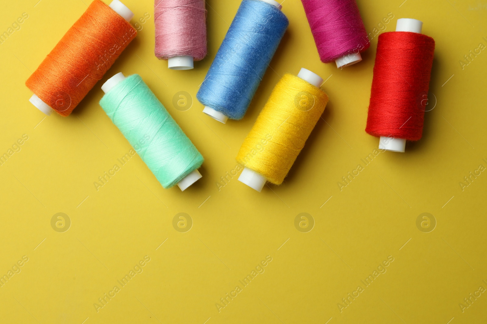 Photo of Different colorful sewing threads on yellow background, flat lay. Space for text