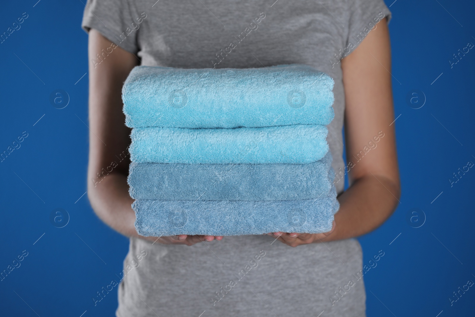 Photo of Woman holding fresh towels on blue background, closeup