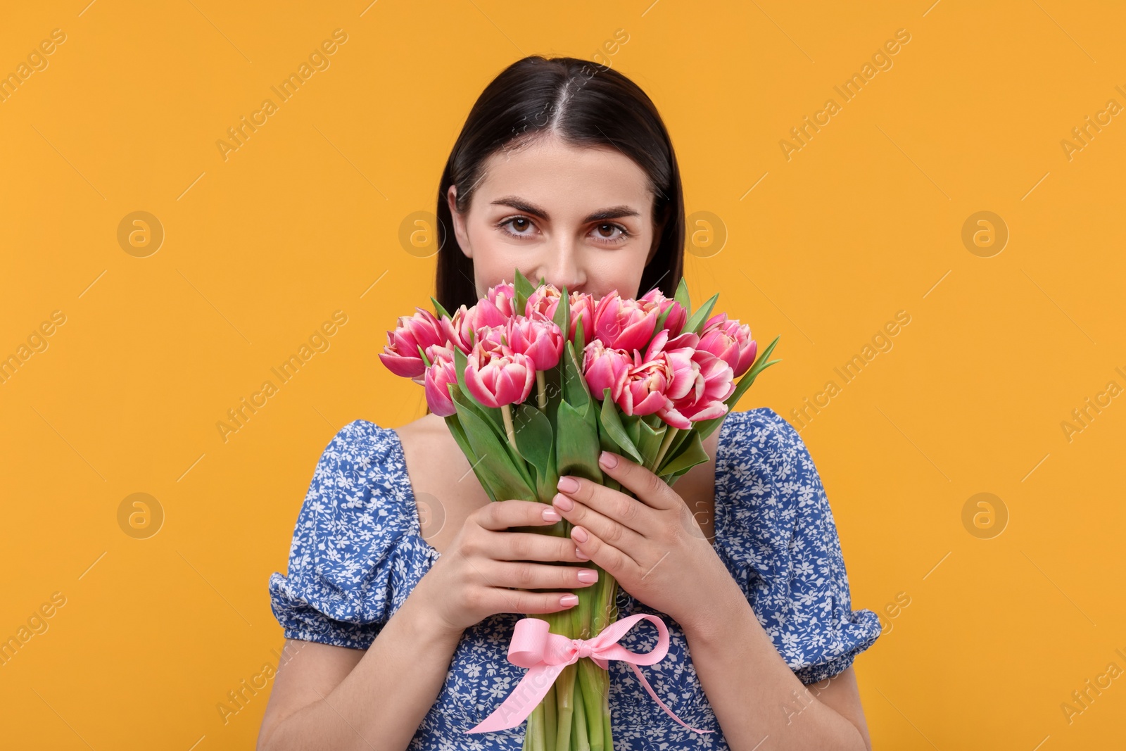 Photo of Happy young woman with beautiful bouquet on orange background