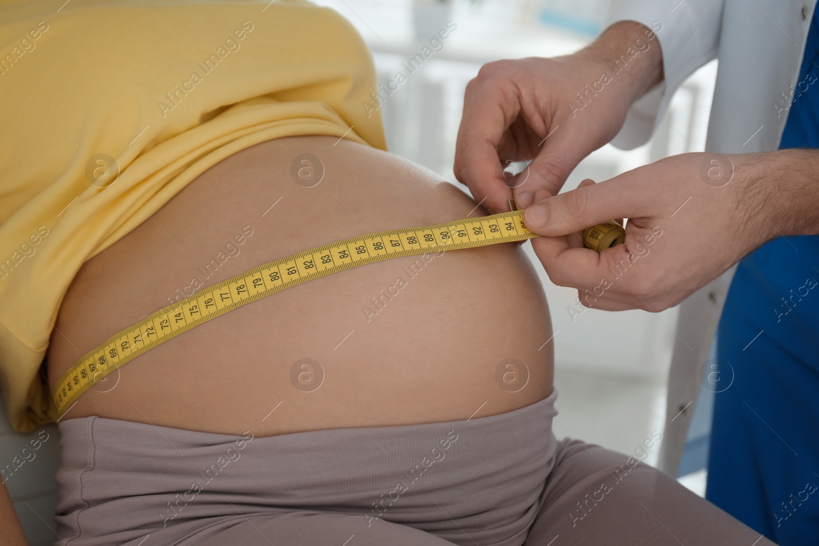 Photo of Doctor measuring pregnant woman's belly with tape in clinic, closeup