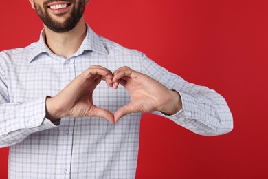 Man making heart with hands on red background, closeup