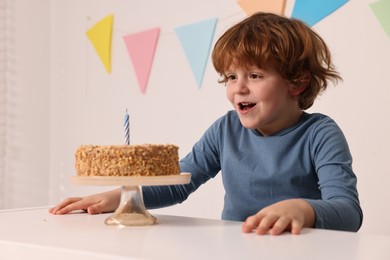 Cute boy with birthday cake at white table indoors