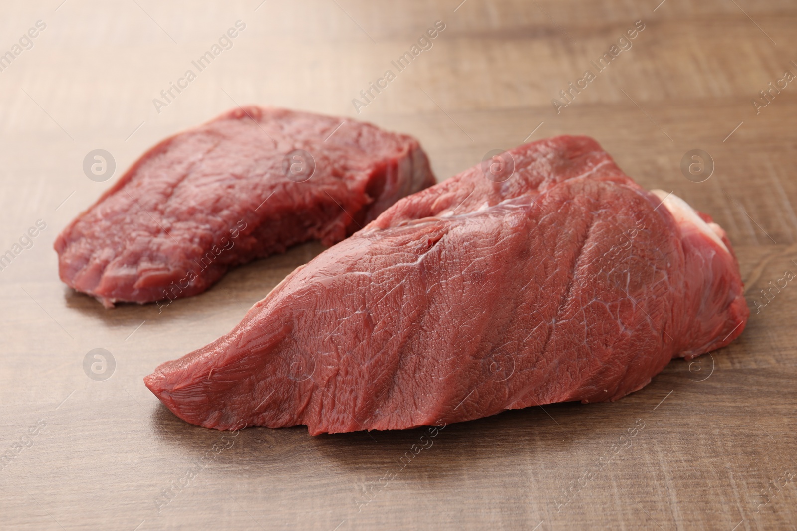 Photo of Pieces of raw beef meat on wooden table, closeup