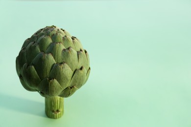 Whole fresh raw artichoke on green background, closeup. Space for text