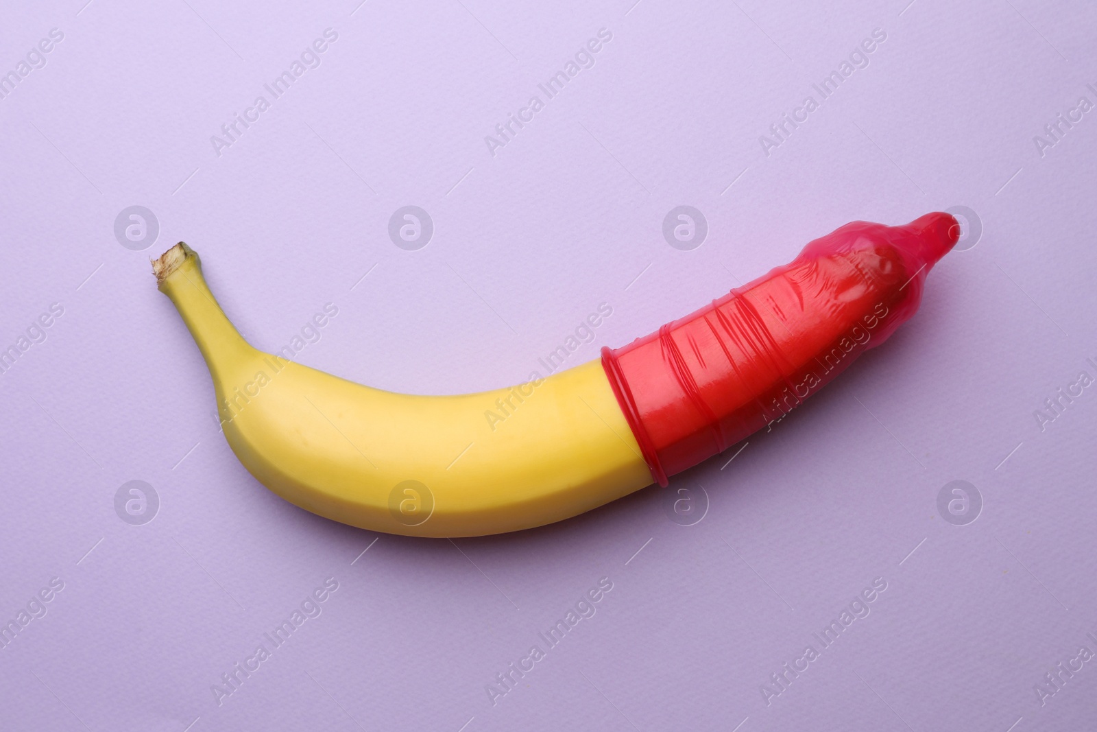 Photo of Banana with condom on lilac background, top view. Safe sex concept