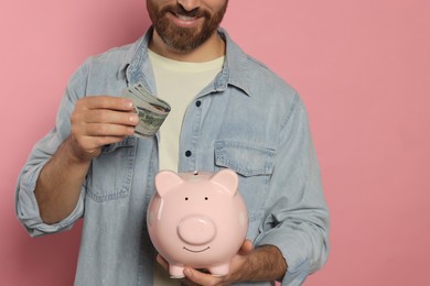 Man putting money into piggy bank on pale pink background, closeup