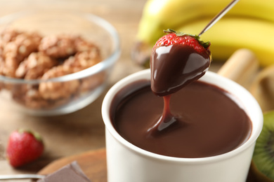 Photo of Dipping strawberry into fondue pot with chocolate, closeup. Space for text