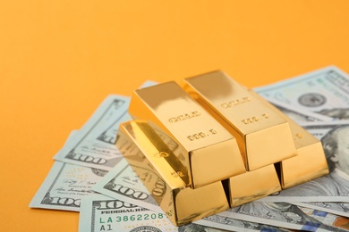 Shiny gold bars and dollar bills on color background