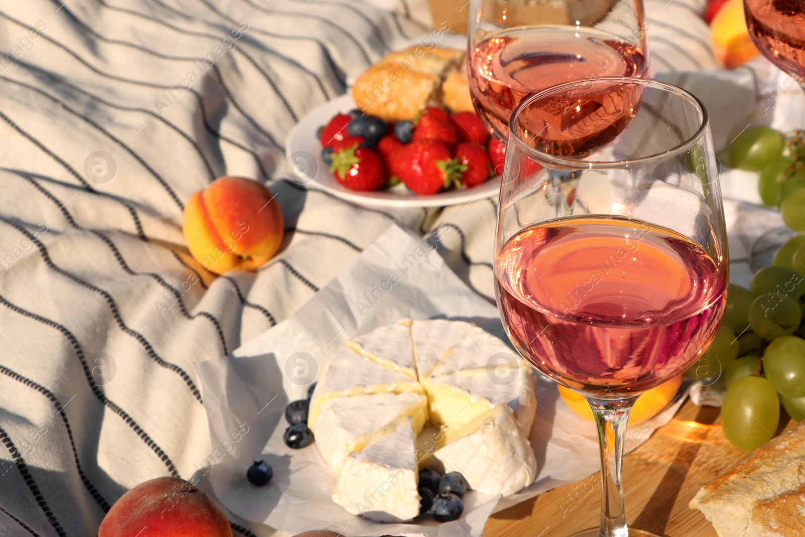 Photo of Glasses of delicious rose wine and food on white picnic blanket, closeup