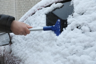 Man cleaning snow from car outdoors on winter day, closeup. Frosty weather