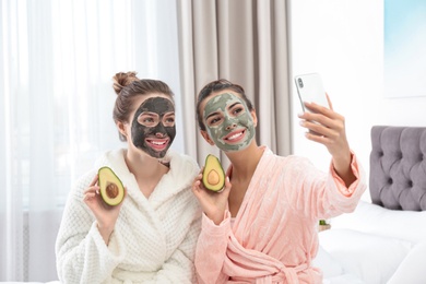 Photo of Young friends with facial masks taking selfie in bedroom at pamper party