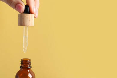 Woman dripping serum from pipette into bottle on pale orange background, closeup. Space for text