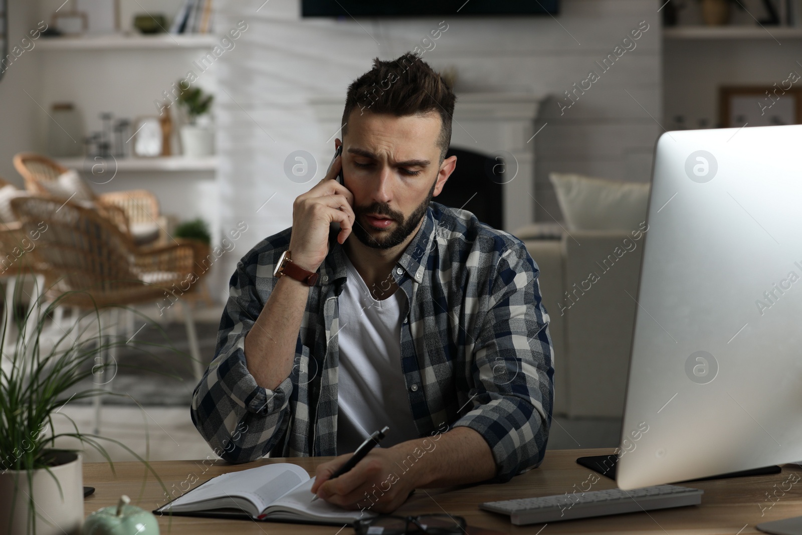 Photo of Man talking on phone while working at table in home office