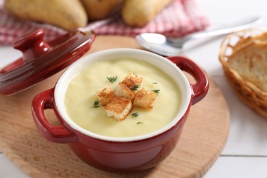 Tasty potato soup with croutons and rosemary in ceramic pot on white table, closeup