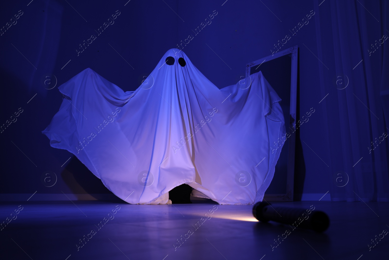 Photo of Creepy ghost. Woman covered with sheet in blue light, low angle view